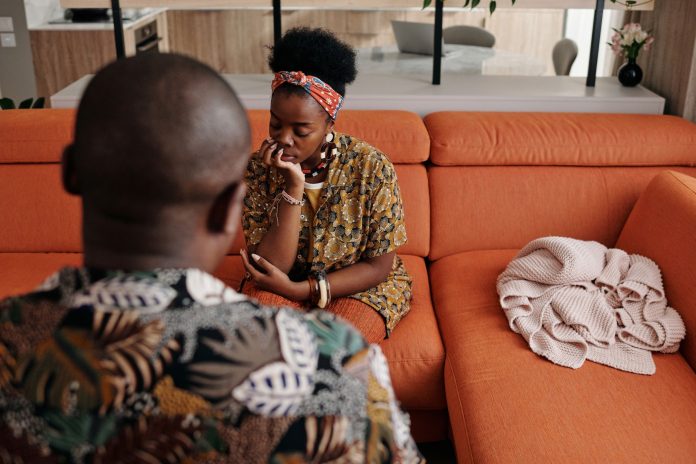 A thoughtful couple engaged in a deep discussion on a vibrant orange sofa in a modern living room.