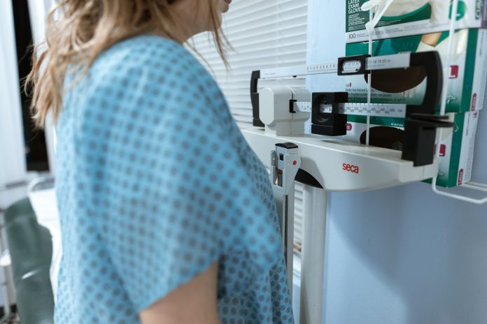 Adult female using a medical weighing scale in a healthcare setting.