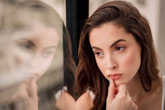 Thoughtful woman sitting by a window, reflecting on negative self-talk