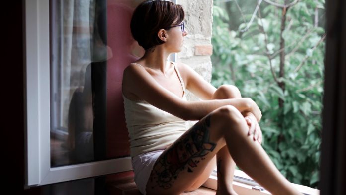 Woman sitting alone by a window looking thoughtful, coping with loneliness