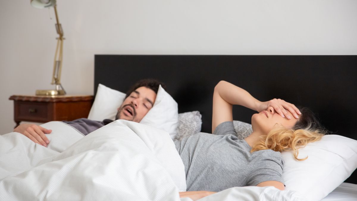 Woman covering her ears while her partner snores in bed, a classic sleep apnea warning sign