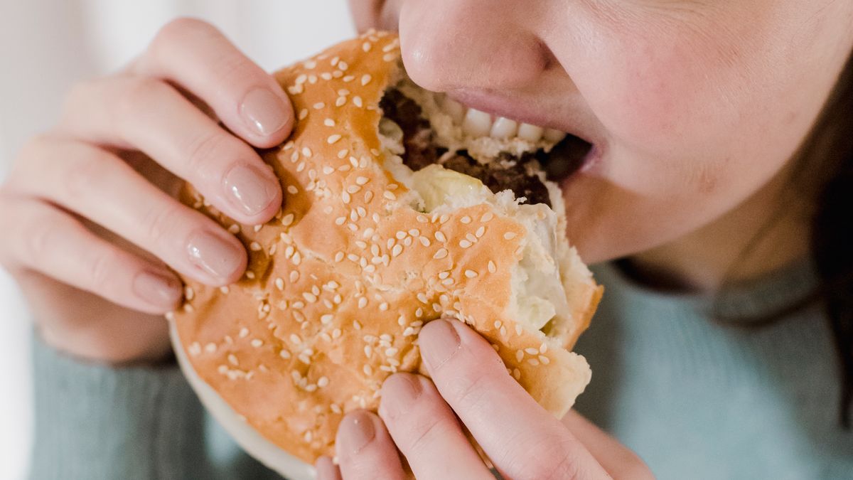Hungry woman eating quickly, a common sign of appetite driven by restriction or stress