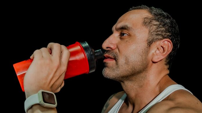 Man drinking a creatine shake from a shaker bottle after a workout