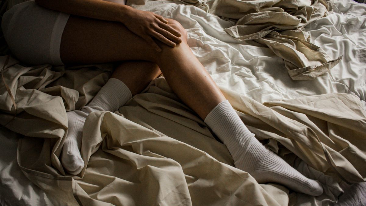 Person in white socks lying on a bed, legs restless at night