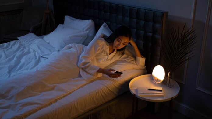 Woman lying awake in a dim bedroom at night with restless legs syndrome