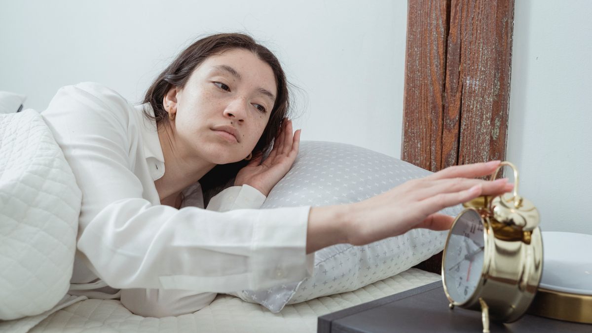 Woman waking up with an alarm clock on a weekday after weekend social jet lag