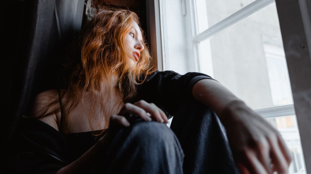 Person sitting on a window sill looking outside, a common experience with emotional numbness