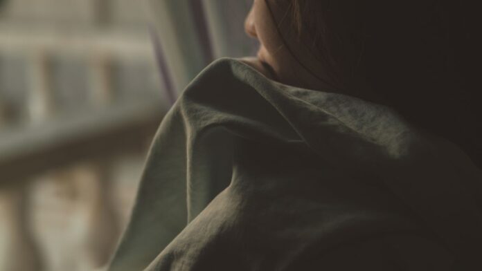 Woman wrapped in a blanket staring out of a window, experiencing emotional numbness