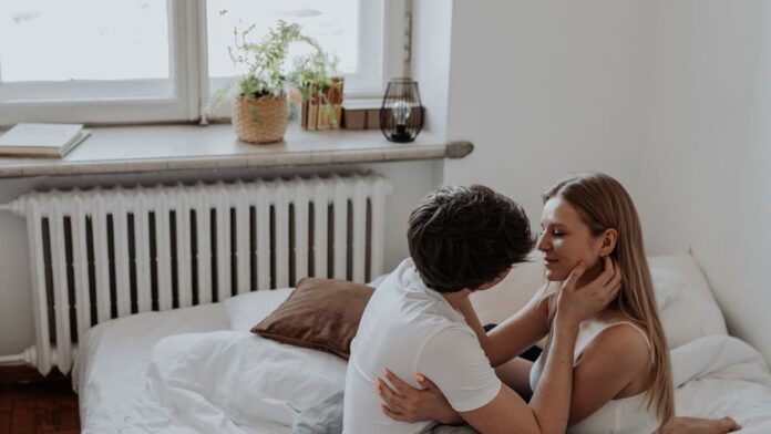 Adult couple sitting on a bed embracing in a sunlit bedroom