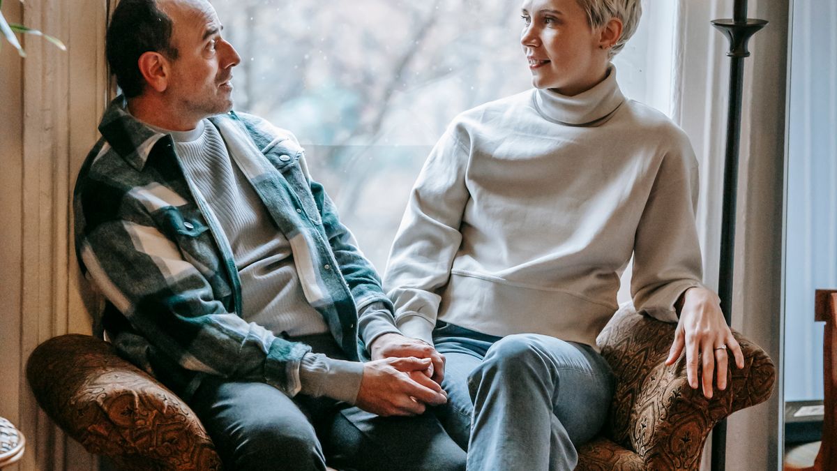 Adult couple sitting close on a couch talking in a sunlit room