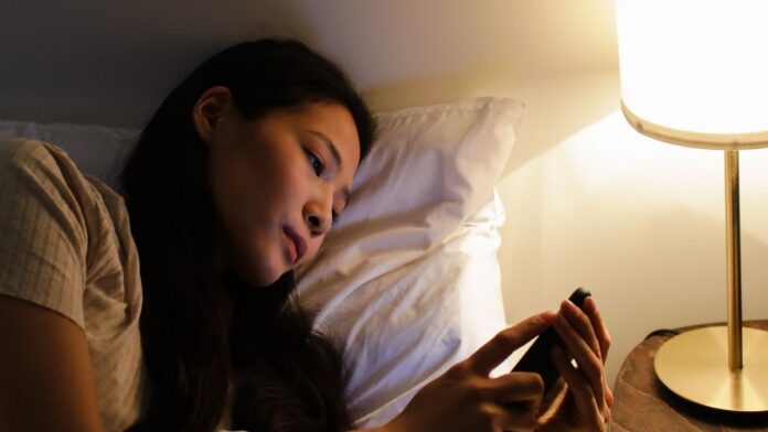 Woman lying in bed at night scrolling her phone, an example of revenge bedtime procrastination