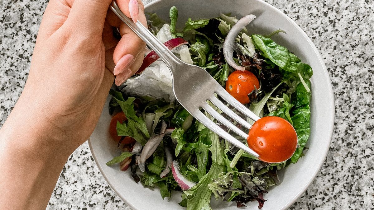 Person eating a fresh vegetable salad with a fork, a high-volume low-calorie meal
