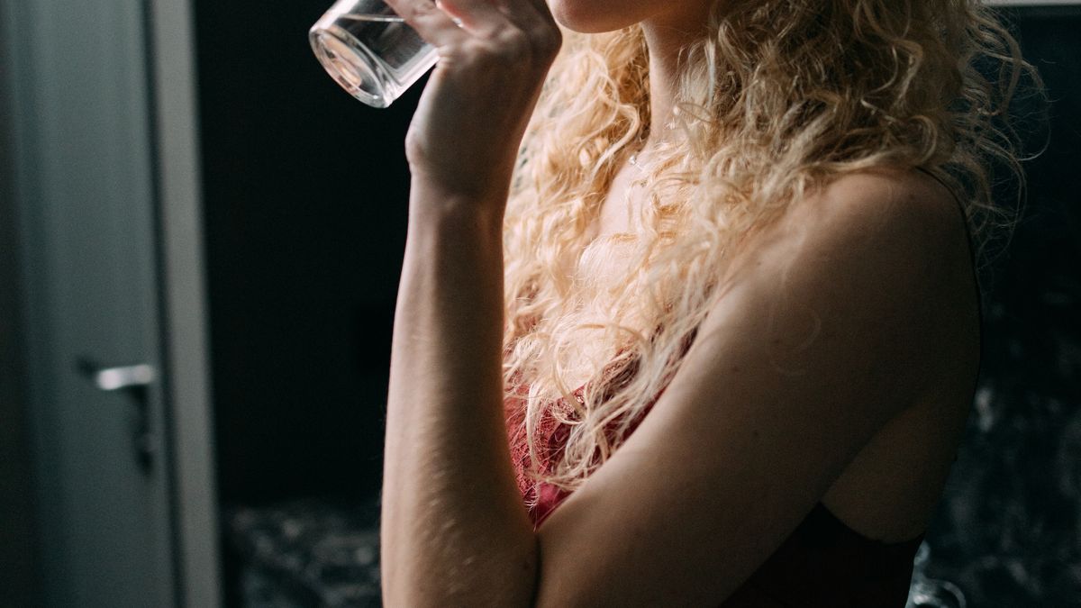 Woman drinking a glass of water in her kitchen to stay hydrated
